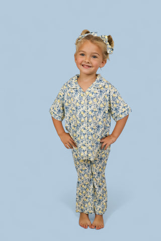 Young girl wearing cream and blue toile print short-sleeve shirt and flared pants with matching hair bows.