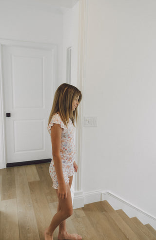Girl wearing white short set with floral print and ruffled short sleeves.