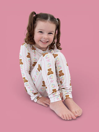 Toddler wearing white long-sleeve pajama top with brown teddy bears and colorful flowers pattern.