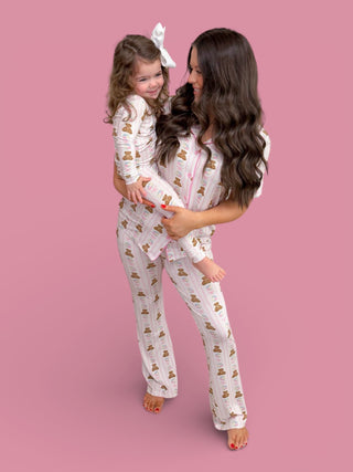Adult and child wearing matching white flare pajama sets with brown bear and flower print on pink background.