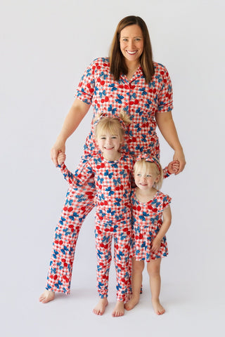 Woman and two children wearing matching red, white, and blue cherry and star print pajama sets with short sleeves and flare p