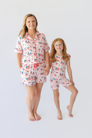 Woman and girl wearing matching short pajama sets with red, white, and blue patriotic print including flags and bows.