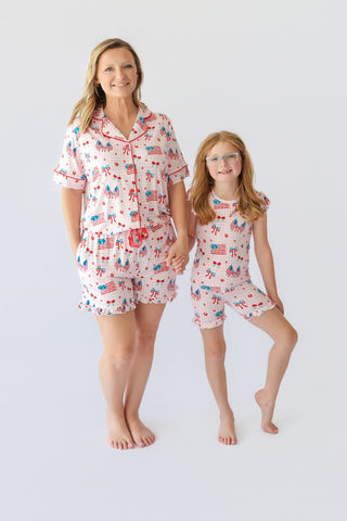 Adult and child wearing matching short pajama sets with red, white, and blue patriotic print including flags and bows.