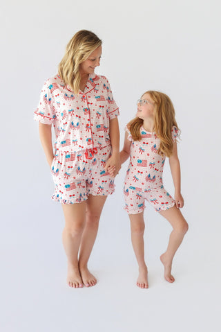 Adult and child wearing matching short sets with red, white, and blue flag and bow print, ruffled short sleeves, and shorts.