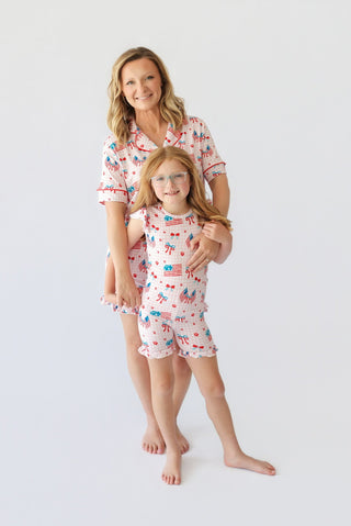 Woman and child wearing matching short pajama sets with red, white, and blue patriotic print including flags and bows.