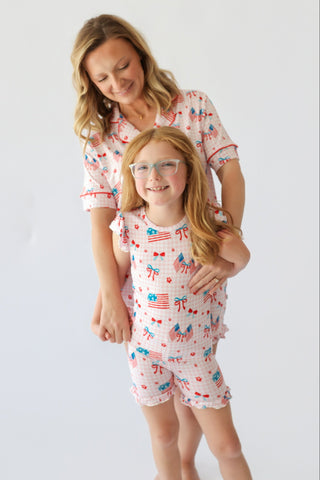 Adult and child wearing matching short sets with red, white, and blue flag and bow print, ruffled sleeves and leg cuffs.