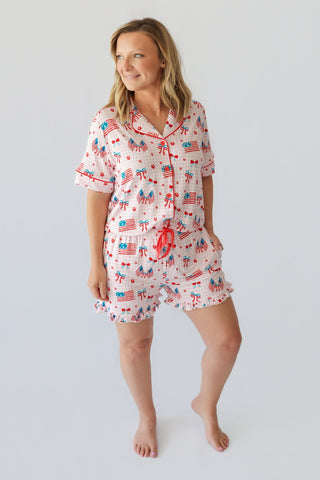 Woman wearing a white short pajama set with red, blue, and American flag patriotic print and red drawstring shorts.