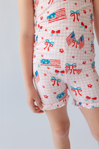 Pink and white gingham shorts with red bows, blue flags, and red flowers printed throughout.