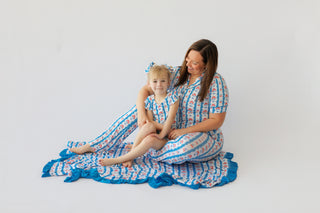 Adult and child wearing matching blue and coral patterned short-sleeve tops and flare pants with ruffled hems.
