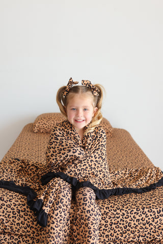 Child wrapped in tan and black leopard print bedding with matching hair accessories and pajamas.