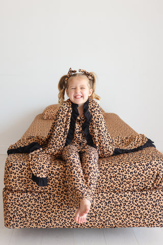 Child wrapped in tan and black leopard print bedding and matching accessory on white background.