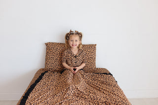 Child sitting on twin bed with tan and black leopard print sheets and matching pillows.