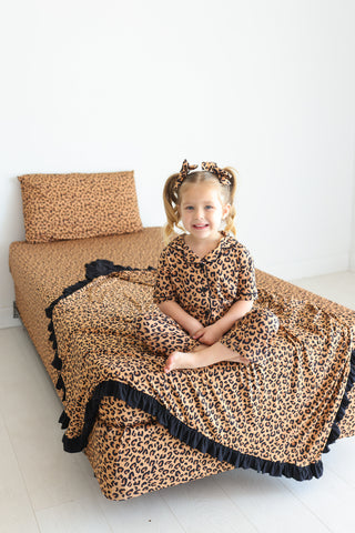 Twin sheet set with tan and black leopard print pattern and black ruffled edges, displayed on bed with pillows.