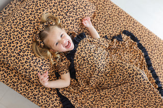 Child lying on tan and black leopard print twin sheet set.