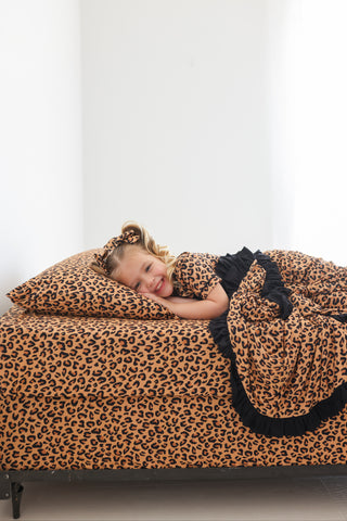 Child on twin bed with tan and black leopard print sheet set and matching pillowcase.
