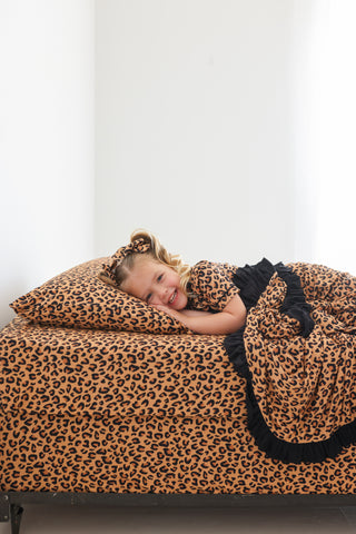 Child resting on tan and black leopard print bedding with matching pillowcase and black ruffle trim.