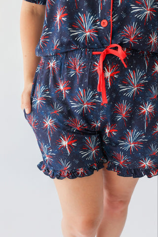 Women's short set with navy fabric featuring red and white firework pattern, red drawstring waist, and button front.