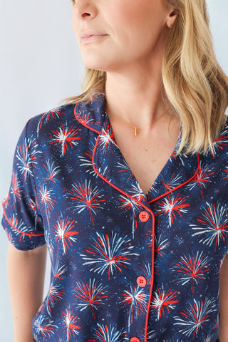 Woman wearing navy short-sleeved top with red, white, and blue firework pattern and red button front closure.