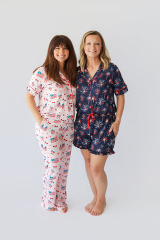 Two women wearing patriotic-themed pajama sets with flag and firework prints in red, white, and navy.