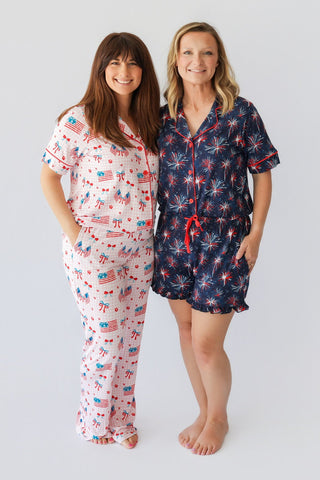 Two women wearing patriotic-themed pajama sets with flag and firework prints in red, white, and navy.