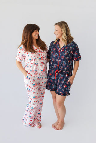 Two women wearing patriotic-themed pajama sets with red, white, and blue prints featuring flags and fireworks.