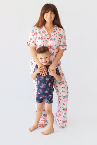 Adult and child wearing matching short sleeve pajama sets with red, white, and blue patriotic print including flags and firew