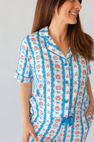 Woman wearing short-sleeve button-up pajama top with blue and coral floral and bow print on cream background.