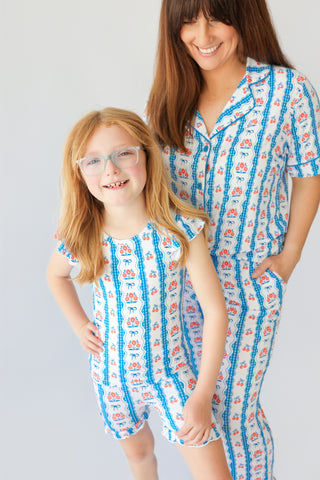 Woman and child wearing matching pajama sets with blue stripes and red floral print on white background.