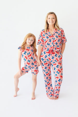 Woman and girl wearing matching pajama sets with red cherries and blue stars print on white background.