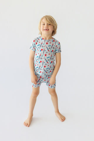 Child wearing short-sleeved shirt and shorts set with red stars, blue rockets, and striped pattern.