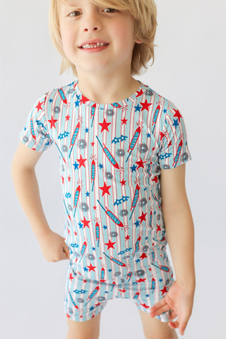 Child wearing short-sleeved shirt and shorts with red stars, blue stars, and rocket print on striped background.