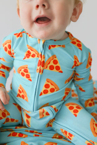 Toddler wearing light blue romper with red and orange pizza slice print and front zipper.