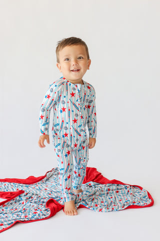 Toddler wearing rocket and star patterned pajamas standing on matching blanket with red trim.