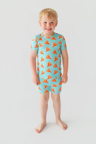 Child wearing turquoise short-sleeved shirt and shorts with repeating orange pizza slice pattern.