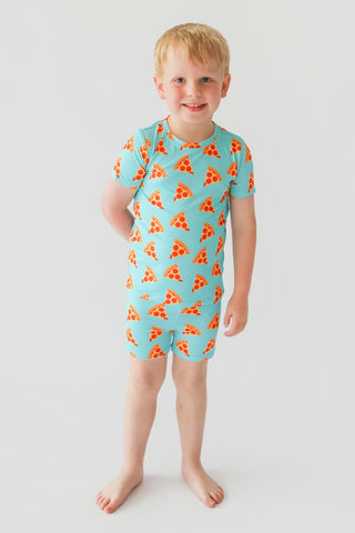 Child wearing turquoise short set with red and yellow pizza slice pattern throughout.