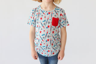 Child wearing short-sleeve tee with red stars, blue rockets, and striped pattern, featuring red chest pocket.