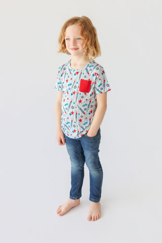 Child wearing short-sleeve tee with rocket and star pattern, red chest pocket, and blue jeans.