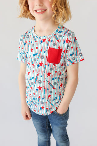Child's short-sleeve tee with red, blue, and gray stars and rockets on white striped background, red chest pocket.