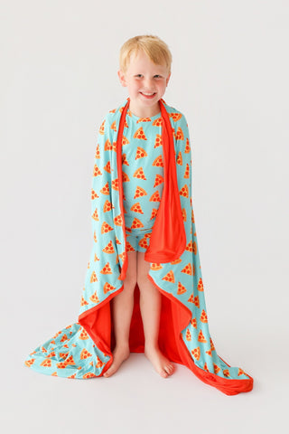 Child wearing light blue short set with orange pizza slice pattern and matching red cape.