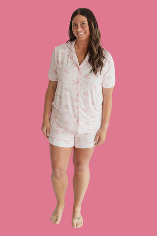 Woman wearing white short-sleeved pajama set with pink floral pattern and button-front shirt with matching shorts.