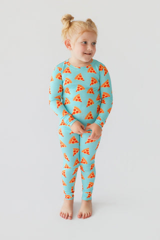 Young child wearing turquoise pajamas with red and orange pizza slice pattern throughout.