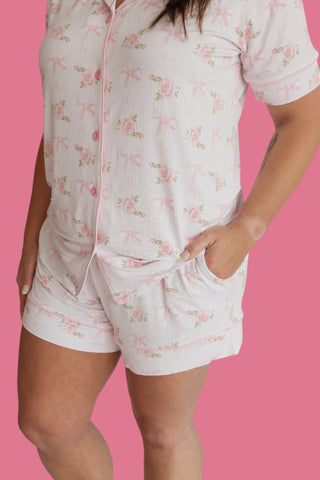 White short pajama set with pink roses and bows, front zip closure, and shorts with pockets.