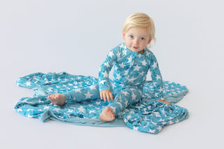 Toddler wearing a blue romper with white star pattern, sitting on matching fabric against a white background.