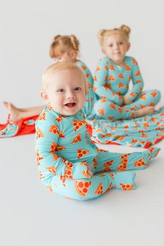 Toddlers wearing turquoise rompers with orange and red pizza slice print pattern.