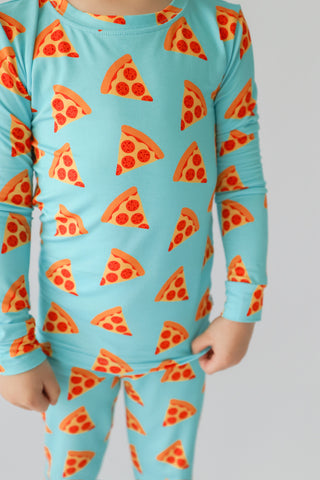 Child wearing turquoise long-sleeve top and matching pants with repeated pizza slice pattern in orange and red.