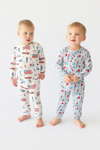 Two toddlers wearing long-sleeve pajama sets with American flag and skateboard prints in red, blue, and white.