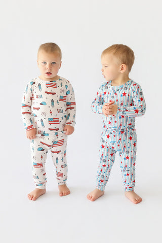 Toddler in two-piece pajama set with skateboard and American flag print shown from front and side views.