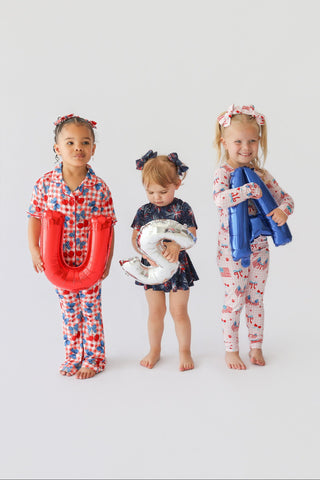 Three young children wearing red, white, and blue patterned pajama sets with coordinating hair bows and accessories.