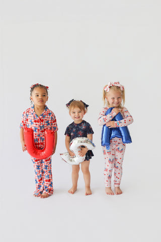 Three young children wearing red, white, and blue patriotic-themed outfits with matching hair bows and accessories.