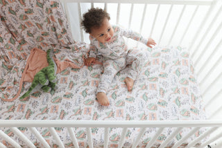Crib sheet with colorful dinosaur and plant pattern in white, pink, and green tones.